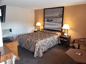Ein Hotelzimmer mit einem großen Bett, zwei Nachttischlampen, einem Schreibtisch mit Stuhl, einem Fernseher und einem gerahmten Bild an der Wand.