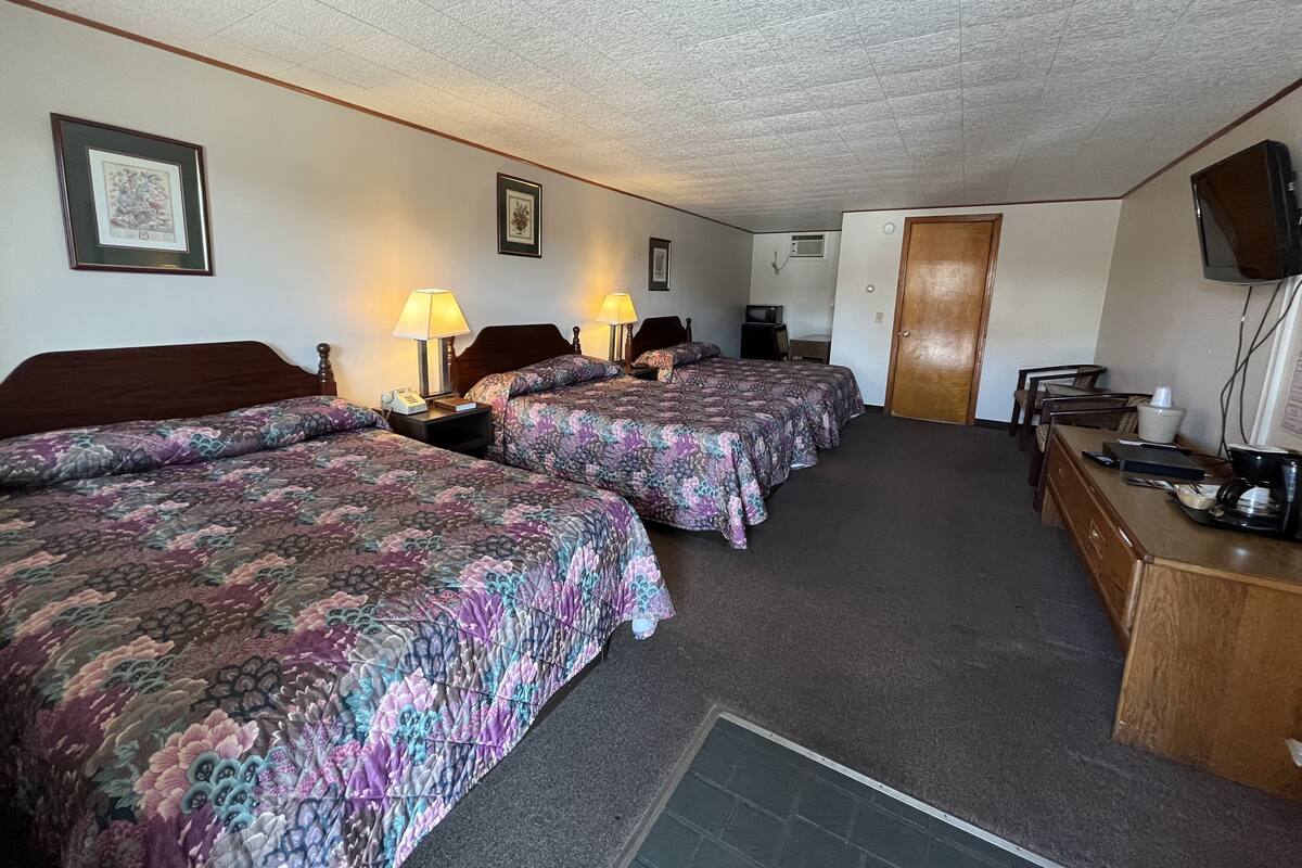 A hotel room with two beds, a desk, a chair, a television, and a door.