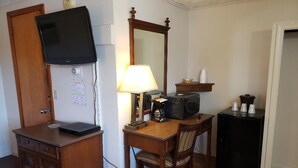Habitació d'hotel senzilla amb escriptori de fusta, televisió penjada a la paret, nevera petita i paperera.