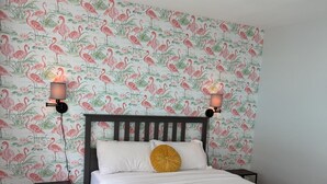 A bedroom with a bed, two bedside lamps, a nightstand, a ceiling fan, and a wall with a floral wallpaper.