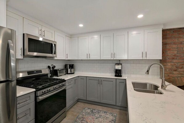 A modern kitchen with white cabinets, stainless steel appliances, and a brick accent wall.