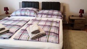 Een tweepersoonsbed met een gestreept sprei en twee kussens, een nachtkastje met een lamp, en een houten nachtkastje met een lamp.