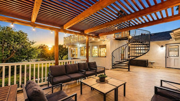 An outdoor patio with a wooden pergola, a sofa, a table, and a spiral staircase.