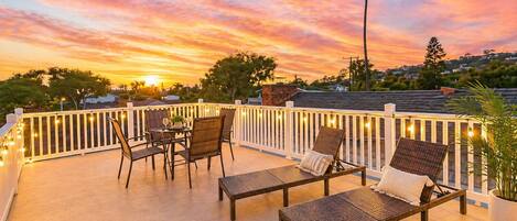 A balcony with wicker furniture, string lights, and a view of the sunset.