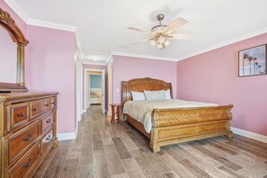 A bedroom with a wooden bed, a dresser, a ceiling fan, and a hallway leading to another room.