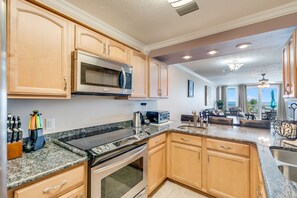 A kitchen with granite countertops, stainless steel appliances, wooden cabinets, and a view to the living area.