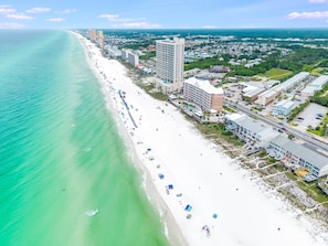 An aerial view of a beachside hotel with multiple buildings, a long stretch of beach, and a clear view of the ocean.