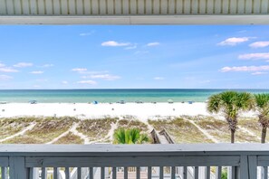 A beach view from a wooden deck with a clear sky and a sandy beach.
