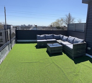 Une terrasse sur le toit, dotée d’un revêtement de sol en gazon synthétique, d’un canapé d’angle et de deux petites tables d’appoint.