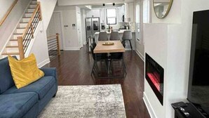 Uma sala de estar moderna com um sofá azul, uma mesa de jantar de madeira e uma lareira.