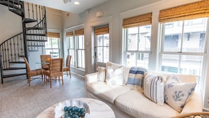 A spacious living area with a white sofa, wicker chairs, a marble coffee table, and a black spiral staircase. - Bunny's Carriage House (Panama City Beach)