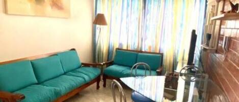 A living room with a sofa, a dining table with chairs, a ceiling fan, and a colorful curtain.