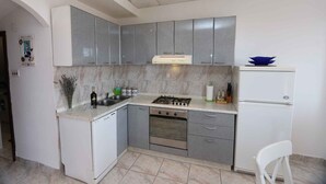 Una cocina compacta con gabinetes grises, encimera blanca, estufa a gas, horno integrado y refrigerador blanco.