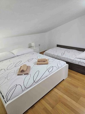 A bedroom with two beds, a wooden floor, and a white wall.