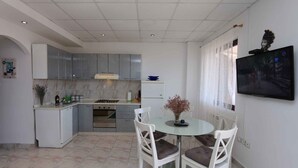 Una cocina moderna con armarios blancos, una mesa de comedor con dos sillas y un televisor montado en la pared.