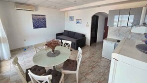 Una cocina moderna con encimera de mármol y armarios blancos, un comedor con mesa y sillas redondas, y un sofá gris.