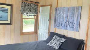 Ein Schlafzimmer mit Bett, Deckenventilator, Tür, Fenster mit Vorhang und einer Wand mit einem Schild.