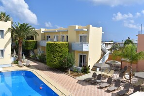 A poolside area with lounge chairs, a swimming pool, and a building with balconies and a staircase. - Mediterranea Apartments (Chania)