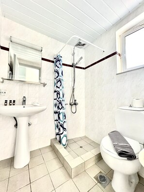 A bathroom with a white sink, a shower with a patterned curtain, and a toilet with a towel on it. - Mediterranea Apartments (Chania)