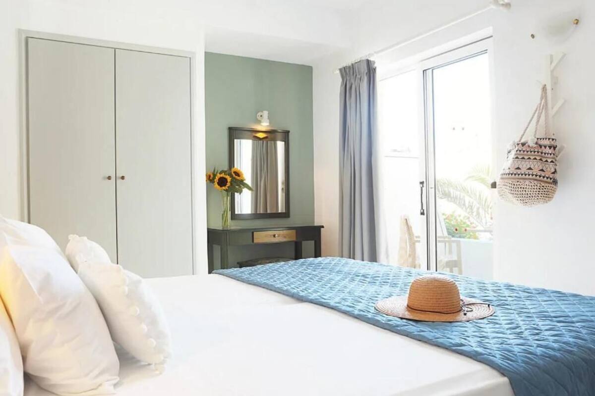 A bedroom with a bed, a dresser, a mirror, and a view of the outdoors.