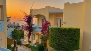 Ein Innenhof mit Blick auf den Sonnenuntergang, umgeben von Gebäuden mit Balkonen und einem gepflegten Garten mit verschiedenen Pflanzen und Blumen.