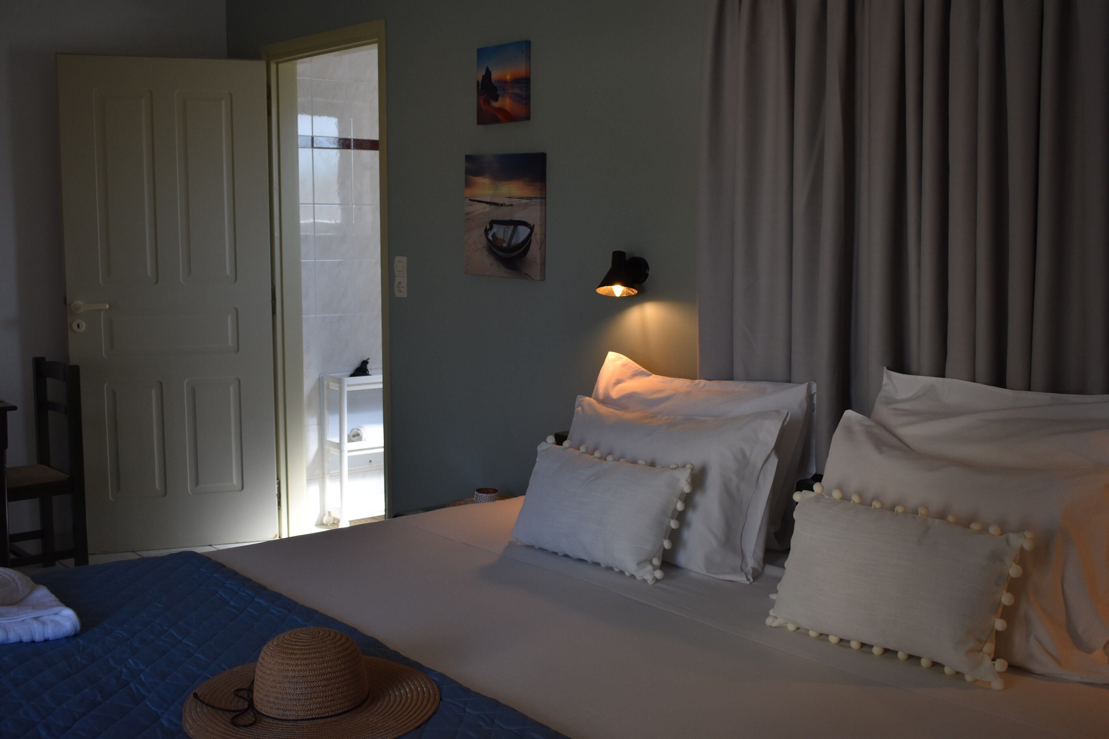 A bedroom with a bed, pillows, a hat, and a wall-mounted lamp.
