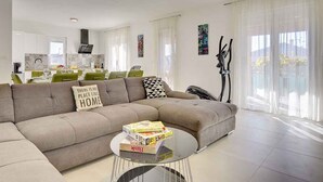 A modern living room with a sectional sofa, a coffee table with books, and a dining area in the background. - Villa with swimming pool and children's playground (Pula)