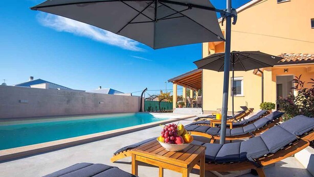A poolside area with lounge chairs, umbrellas, and a table with fruit. - Villa with swimming pool and children's playground (Pula)