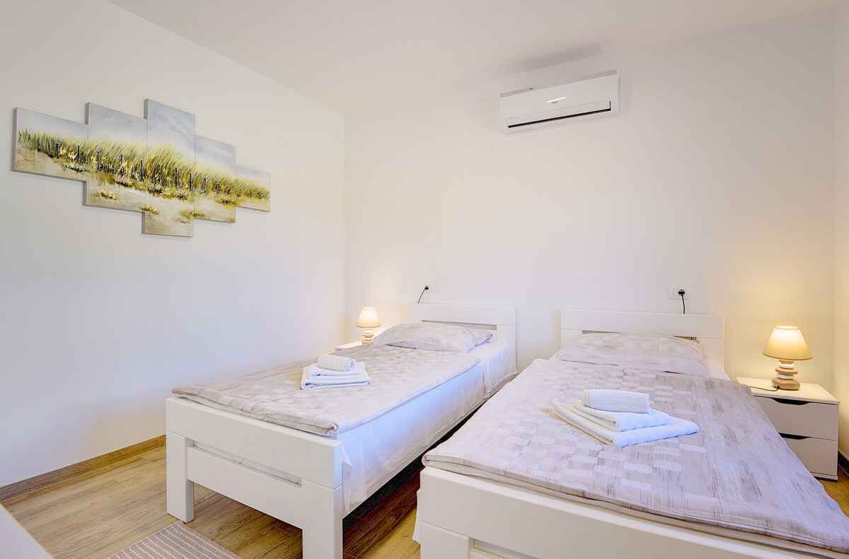A room with two single beds, a wall-mounted air conditioner, and a painting.