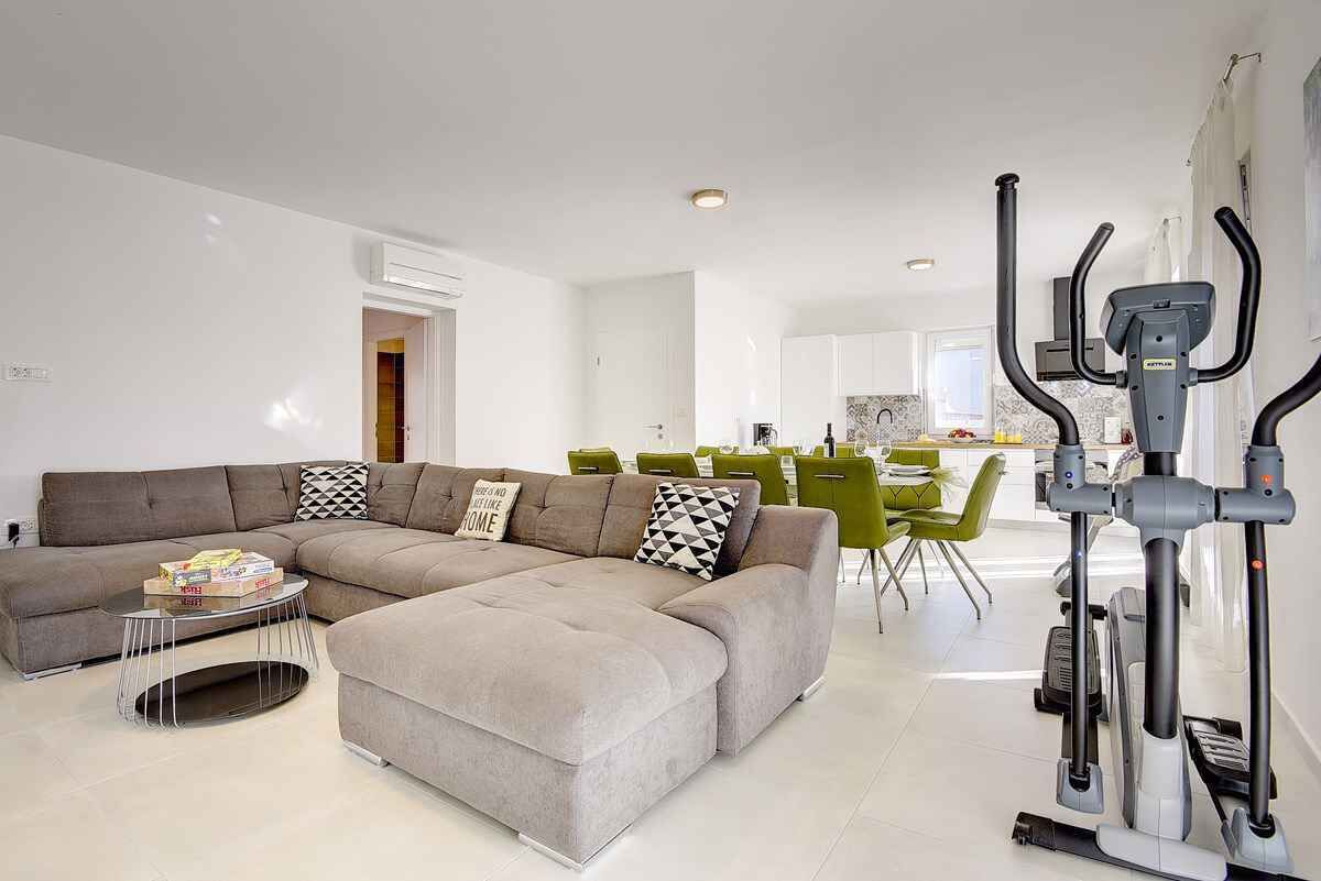 Een moderne woonkamer met een hoekbank, een salontafel en een trainingsapparaat.
