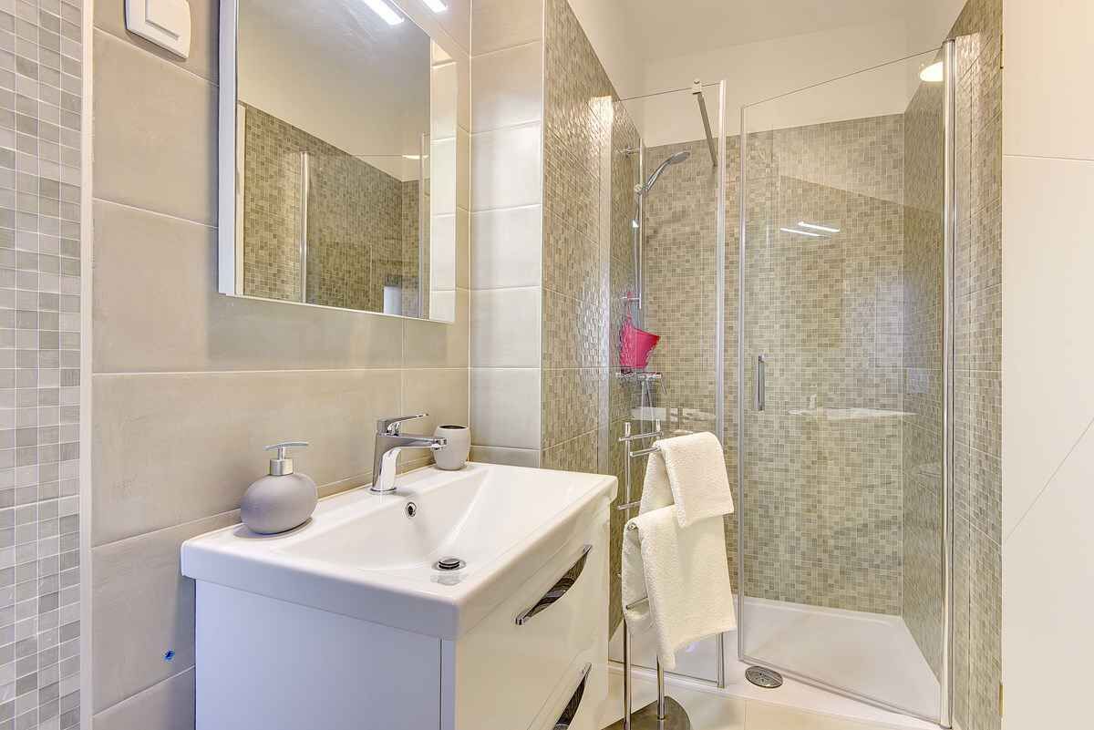A modern bathroom with a white sink, a mirror, and a glass-enclosed shower.