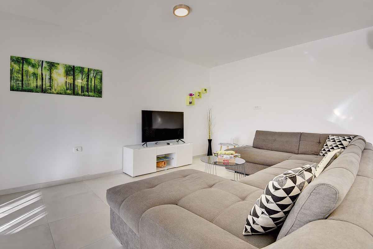 Una sala de estar moderna con un sofá grande, un televisor de pantalla plana y un cuadro de un bosque.