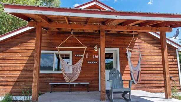 Una cabaña de madera con un porche, dos hamacas, un banco y una puerta con el número 189.
