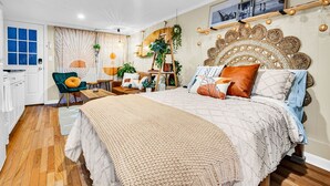 Un dormitorio moderno con una cama grande, un escritorio y una silla. Hay plantas, una escalera y una estantería con fotos.
