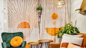 Una habitación con un sillón de terciopelo verde, un sofá marrón y una pequeña mesa de madera.