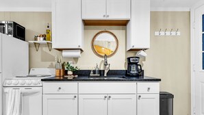 Una cocina moderna con gabinetes blancos, encimera negra, estufa, lavaplatos y cafetera.