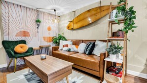 Una sala de estar moderna con un sofá de cuero, una mesa de centro de madera, un sillón verde y una tabla de surf colgada en la pared.