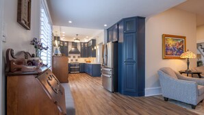 A modern kitchen with dark blue cabinets, a wooden countertop, and a dining area with a gray upholstered chair. - Hickory House Bed & Breakfast (Hickory)
