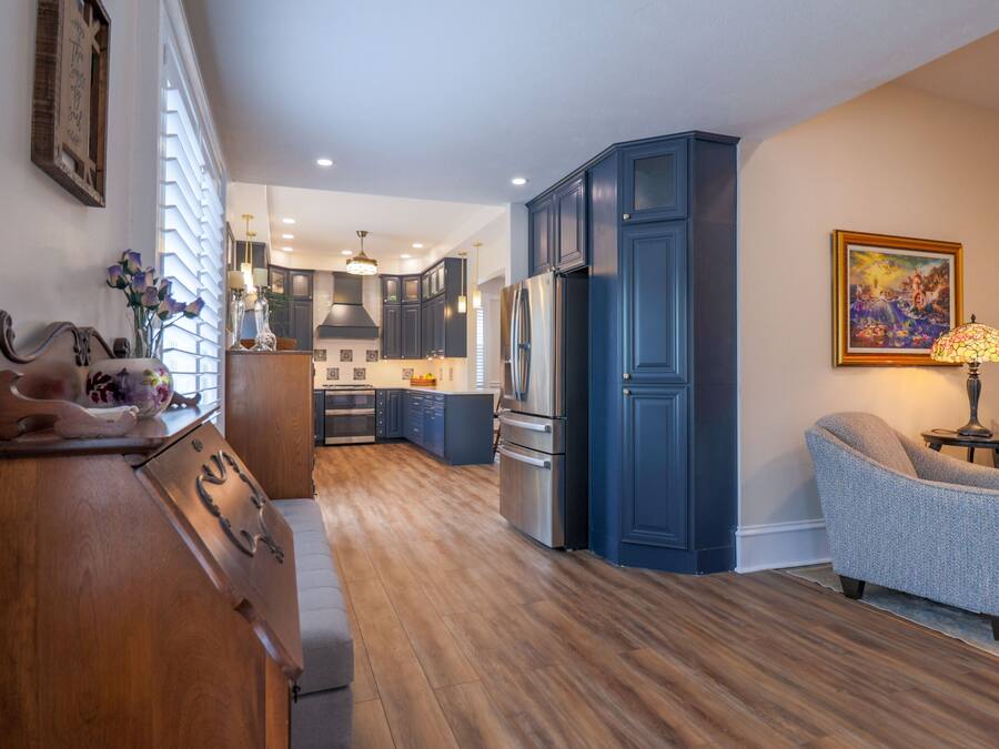 Una cucina moderna con mobili blu scuro, un piano di lavoro in legno e un'area pranzo con una sedia rivestita di grigio.