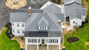 A large, two-story house with a grey shingled roof, a stone foundation, and a front porch with columns. - Hickory House Bed & Breakfast (Hickory)