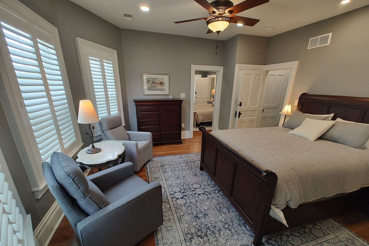 A bedroom with a large bed, a desk, a chair, a dresser, and a ceiling fan.
