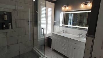A modern bathroom with a glass-enclosed shower, a large vanity with a mirror, and a tiled floor.