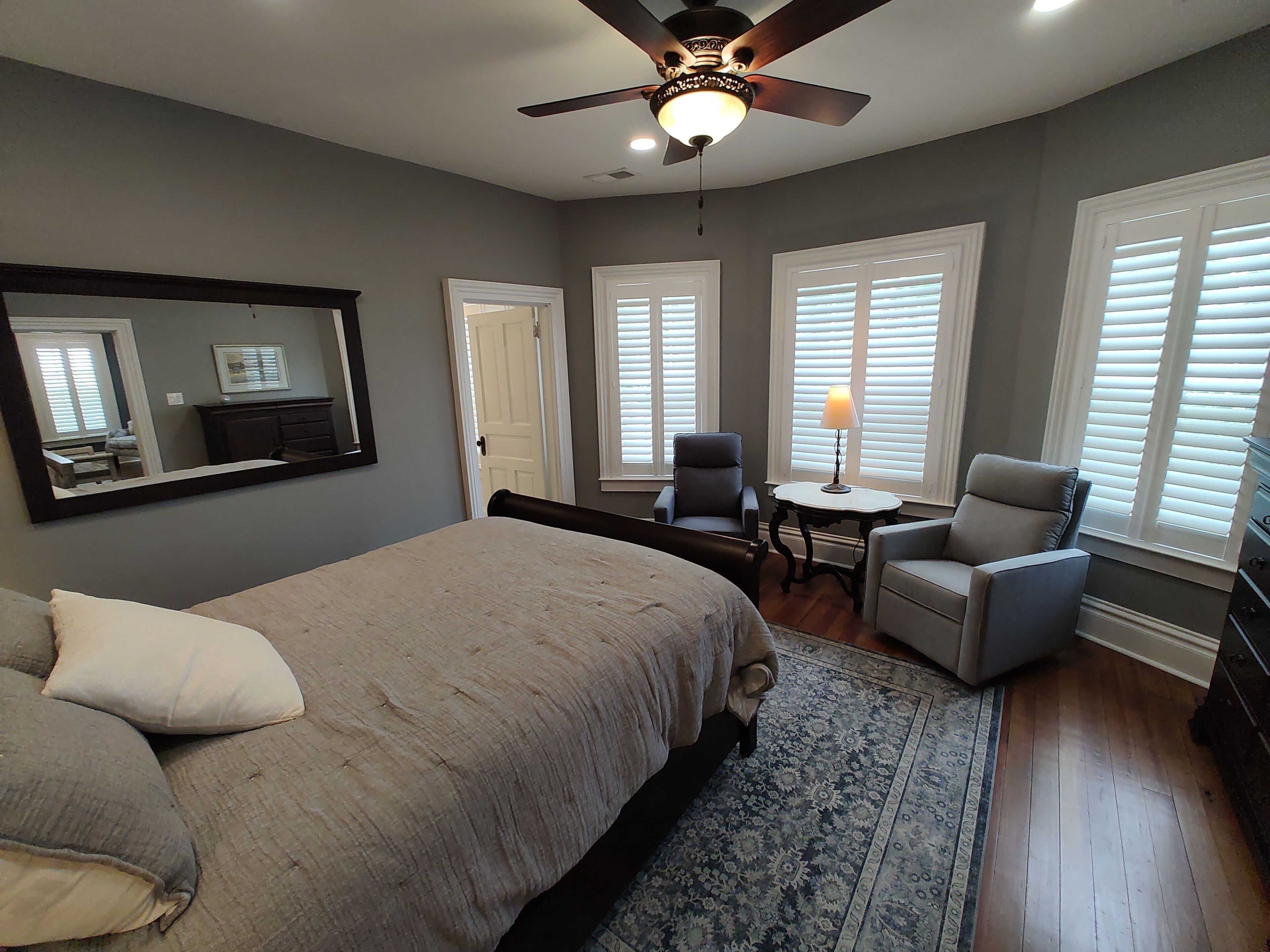 A bedroom with a bed, a ceiling fan, a desk with a chair, and a window with blinds.