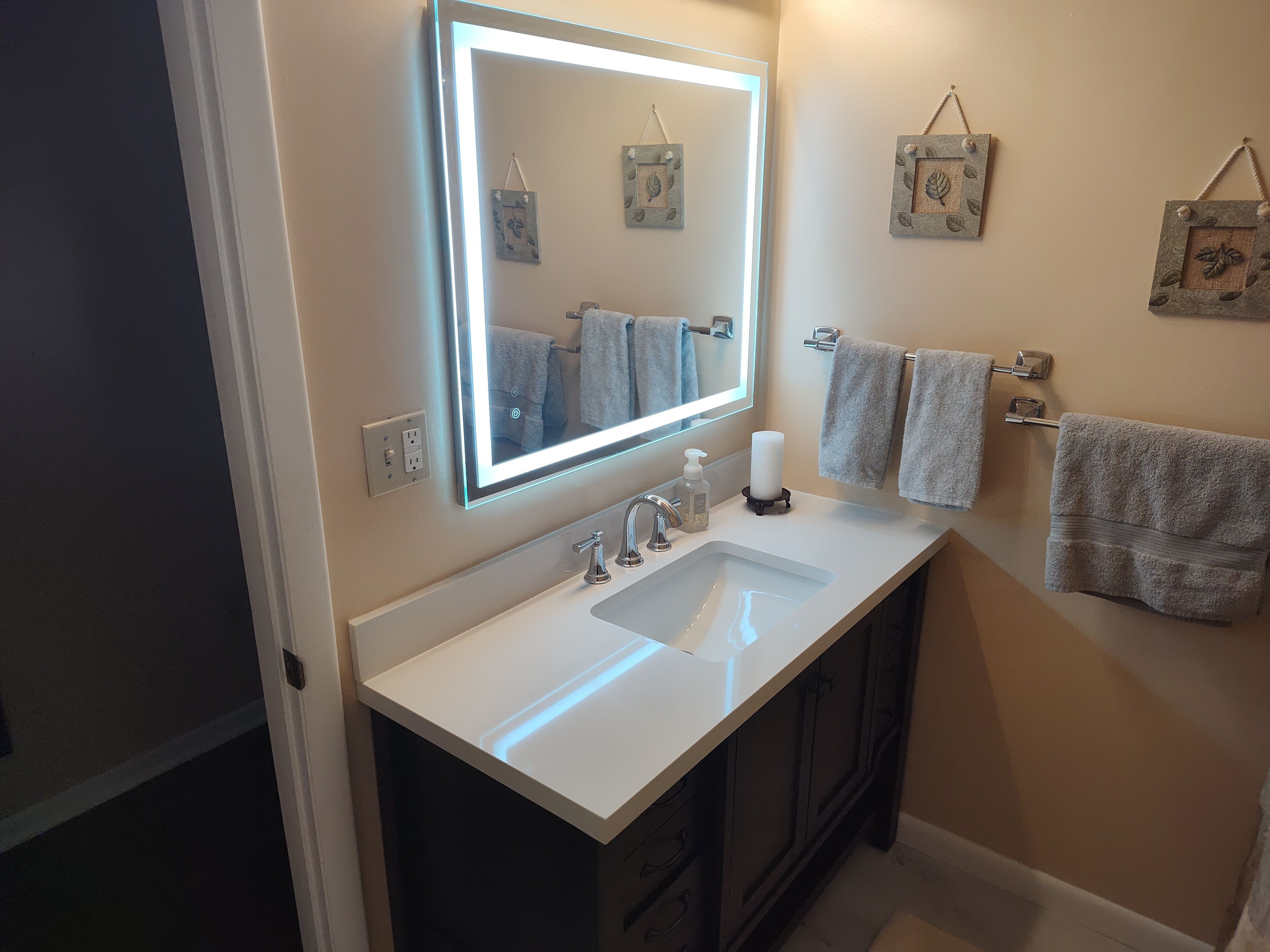 A bathroom with a white sink, a mirror with a light, and towels on a rack.
