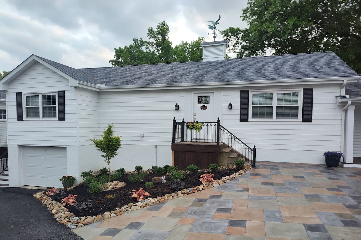 A single-story house with a front porch, a garage, and a landscaped garden with various plants and a stone pathway.