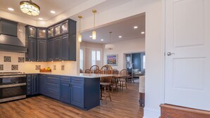 A spacious kitchen with dark blue cabinets, a central island, and a dining area with wooden chairs. - Hickory House Bed & Breakfast (Hickory)