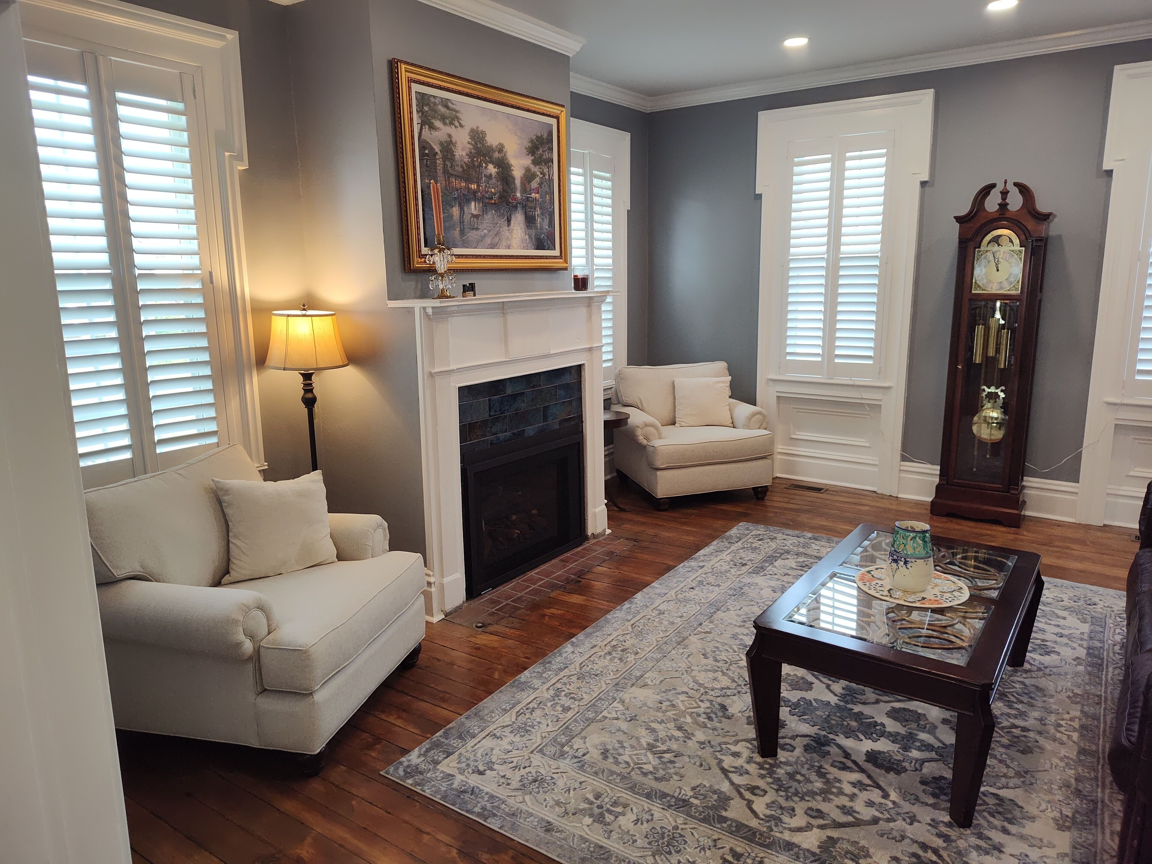 A living room with a fireplace, a sofa, a chair, a coffee table, and a grandfather clock.