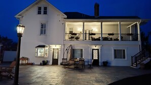 A two-story white house with a balcony, stone patio, and outdoor furniture. - Hickory House Bed & Breakfast (Hickory)