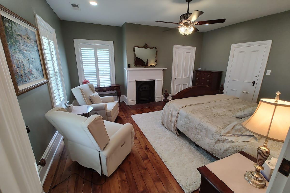 A bedroom with a bed, a chair, a fireplace, and a ceiling fan.