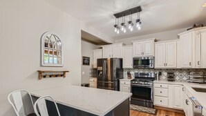 A kitchen with white cabinets, stainless steel appliances, a marble island, and a wooden dining table with chairs.